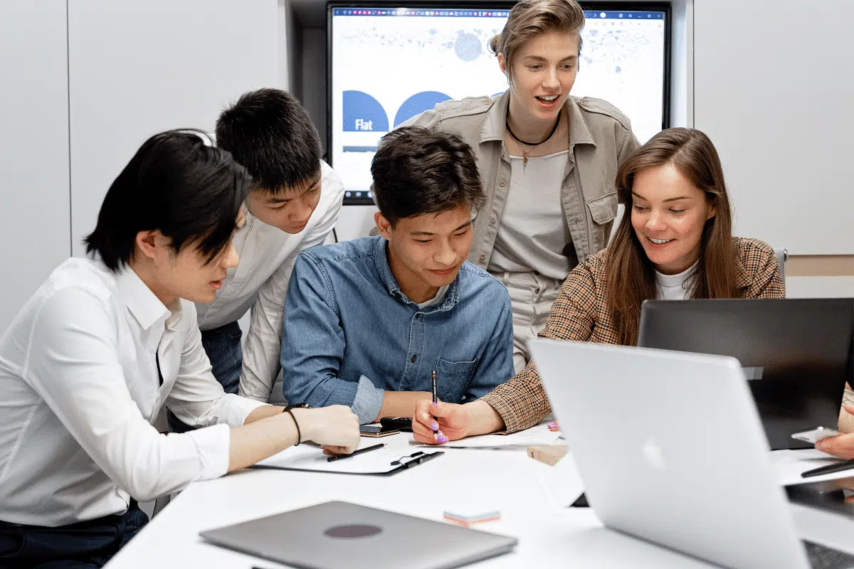 Cinco jovens reunidos em uma mesa de trabalho elaborando projeto de startup, adquirindo habilidades em cursos online