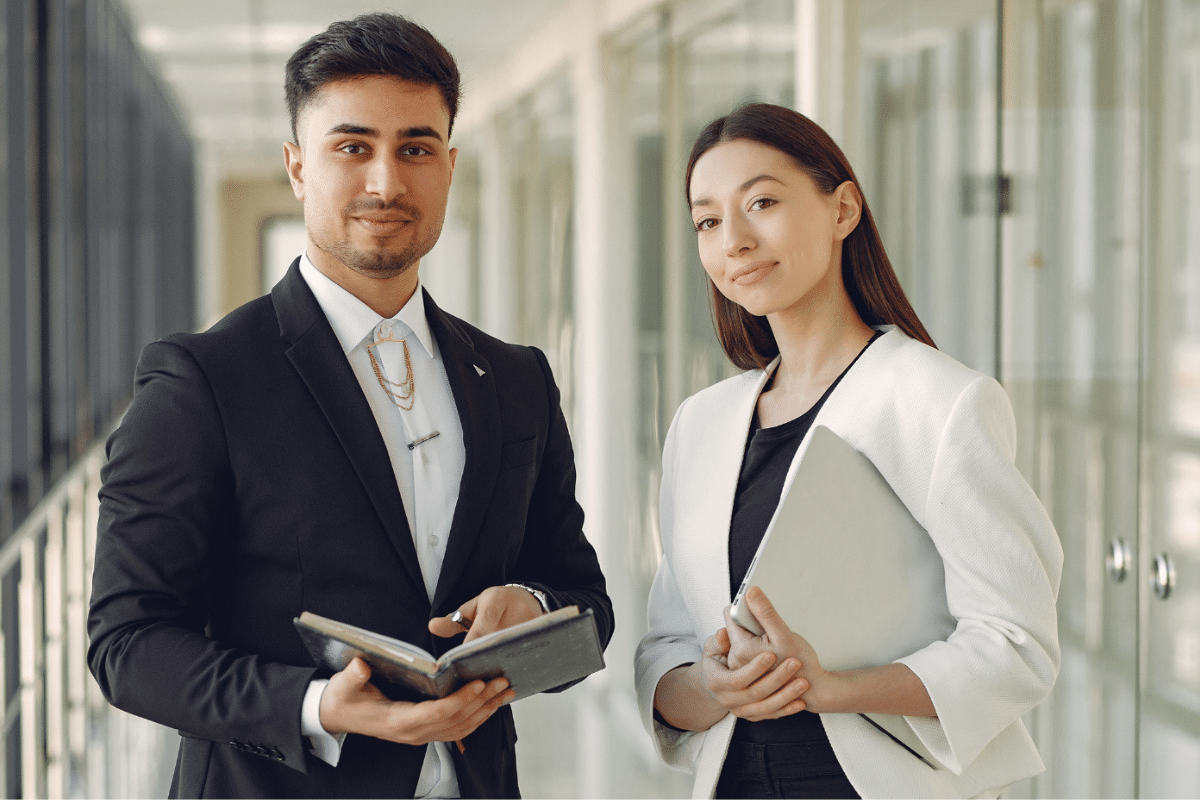 Jovens profissionais sorridentes, homem e mulher, em ambiente corporativo após concluírem cursos que mais empregam, vestindo roupas sociais e prontos para o mercado de trabalho