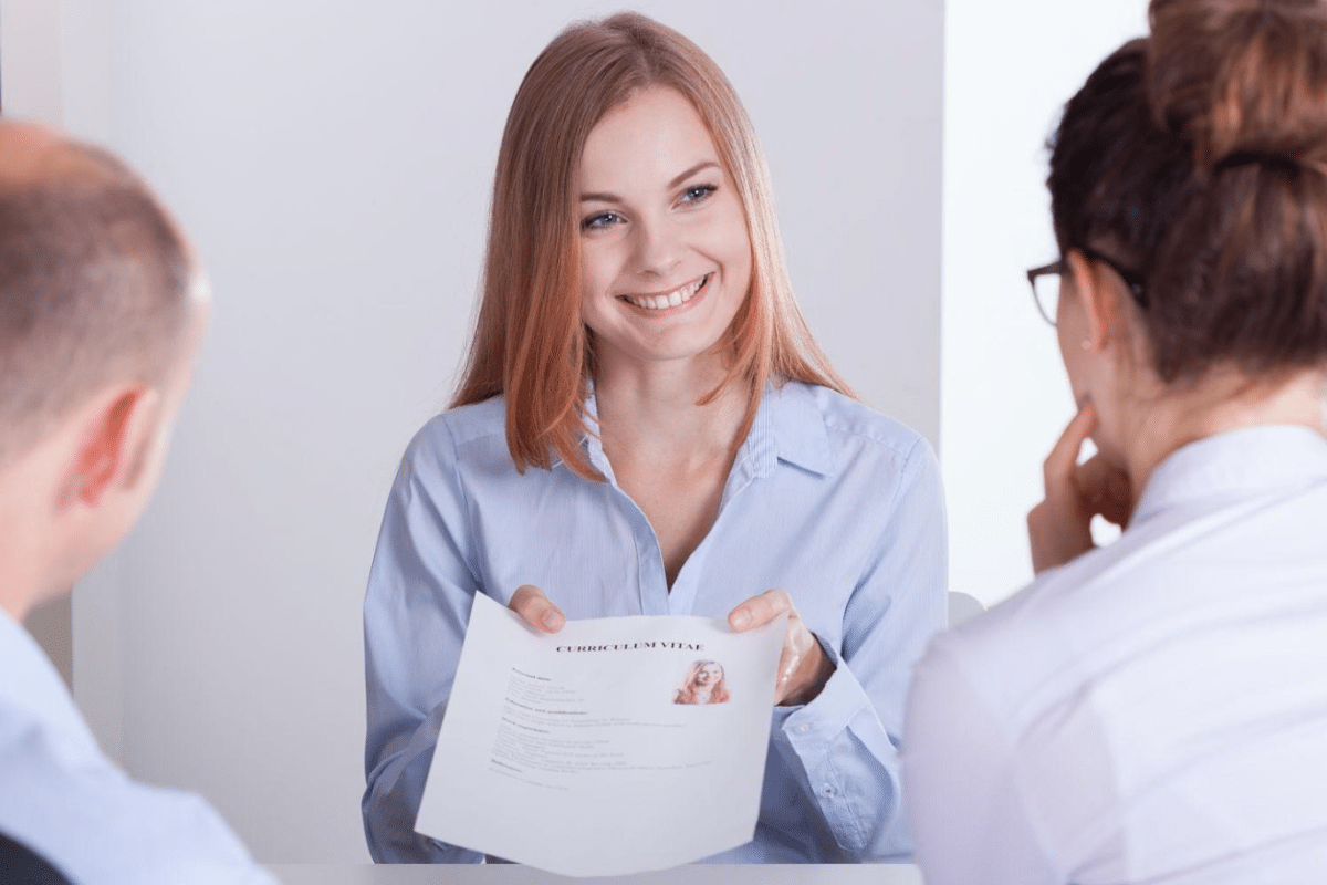 Jovem mulher sorridente entregando currículo em entrevista de emprego, uma das etapas para quem se qualifica com cursos que mais empregam no mercado de trabalho